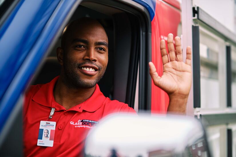 man sitting inside a van waving and arriving to building for door closer repair service